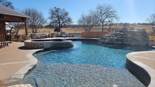A clear swimming pool with a stone edge, surrounded by a wooden deck and a stone wall. - Private Retreat with Pond, Pool and Hot Tub (Boyd)