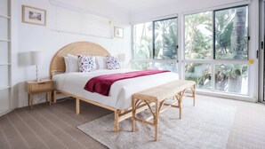 Une chambre à coucher comprenant un lit, une table de chevet, un banc et de grandes fenêtres donnant sur un paysage verdoyant.