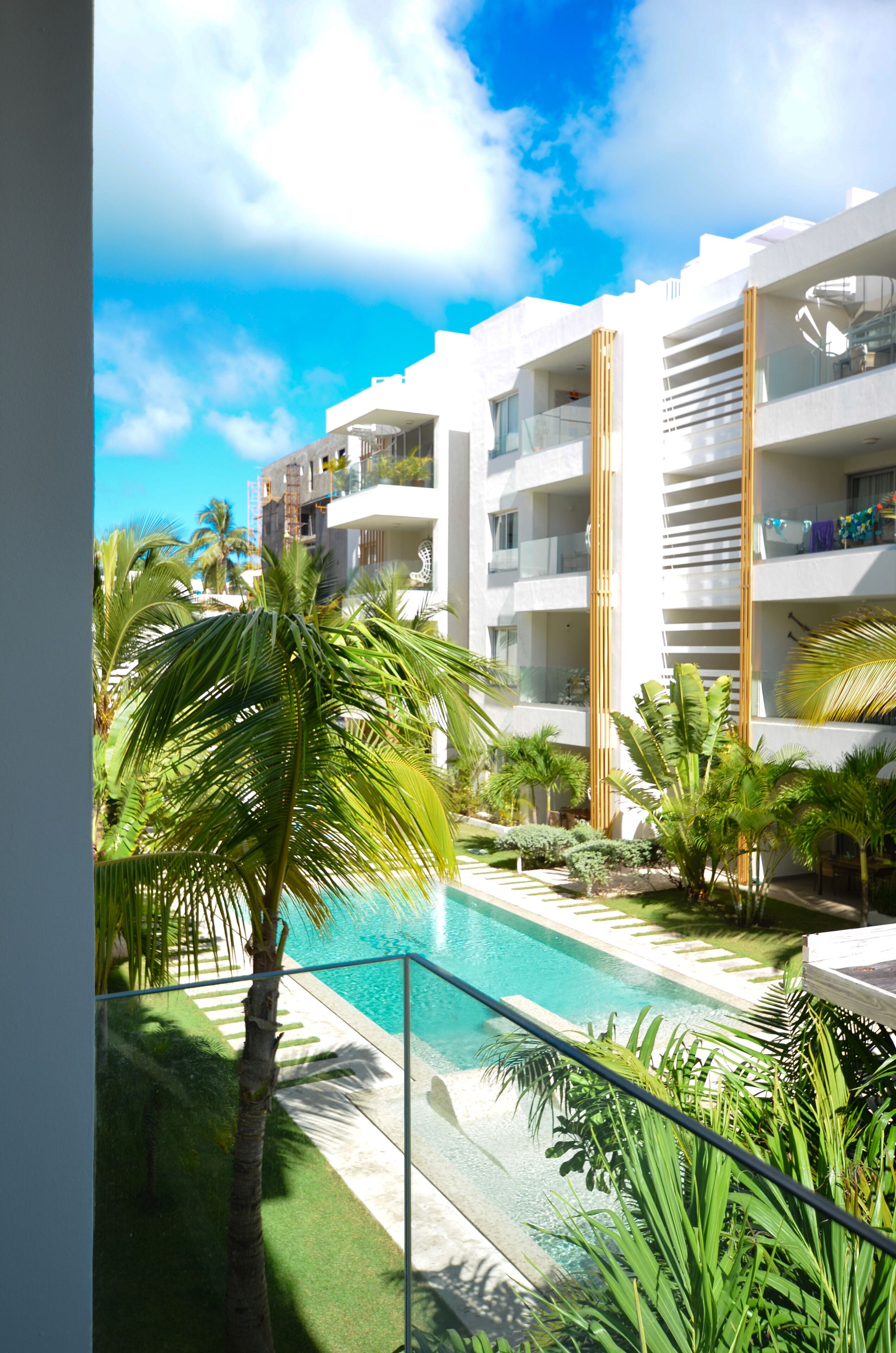 A modern hotel with a pool, palm trees, and a clear blue sky.