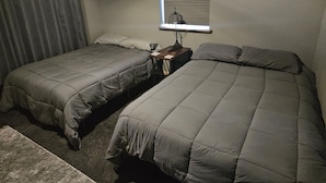 Un dormitorio con dos camas, una ventana con persianas, una mesita pequeña y un adorno en la pared.