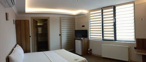 A bedroom with a bed, a TV, a radiator, and a window with blinds.