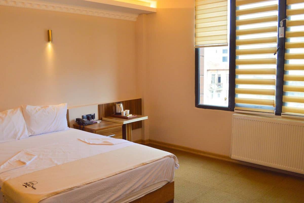 Ein Hotelzimmer mit Bett, Nachttisch, Fenster mit Jalousien und Heizkörper.