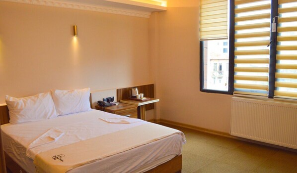 Una habitación de hotel con una cama, una mesita de noche, una ventana con persianas y un radiador.