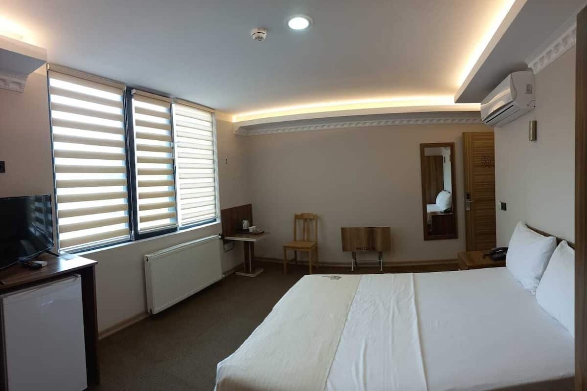 Ein Hotelzimmer mit Bett, Schreibtisch, Stuhl, Fernseher und einem Fenster mit Jalousien.