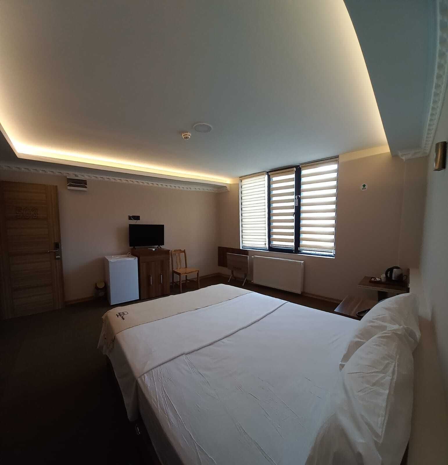 Habitación de hotel con una cama grande, televisión, escritorio y ventana con persianas.