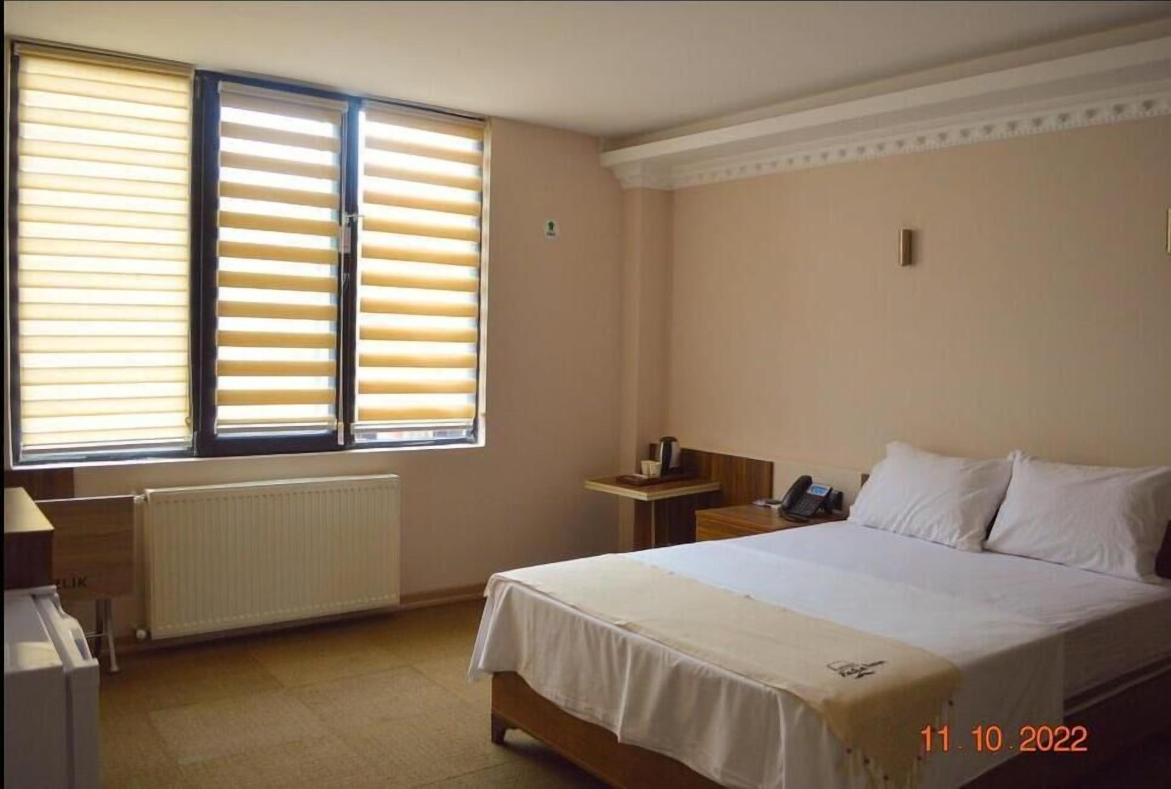 Een hotelkamer met een bed, nachtkastje, radiator en raam met zonwering.