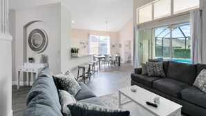 A spacious living area with a grey sofa, a white coffee table, and a dining area with a white table and chairs.