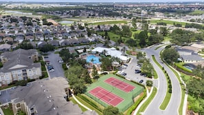 An aerial view of a residential area with a swimming pool, tennis courts, and a curved road.