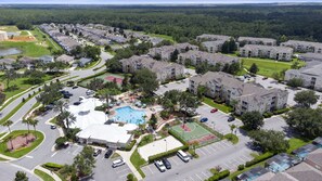 An aerial view of a residential area with apartment buildings, a swimming pool, tennis courts, and a parking lot.