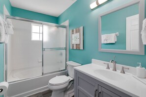 Un baño con ducha envuelta en vidrio, inodoro blanco, tocador con lavamanos y espejo.