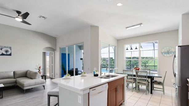 Una cocina moderna con una isla central, un comedor con mesa y sillas, un sofá y un refrigerador.