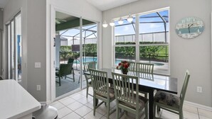 Un comedor con una mesa de vidrio, sillas y vista a una piscina.