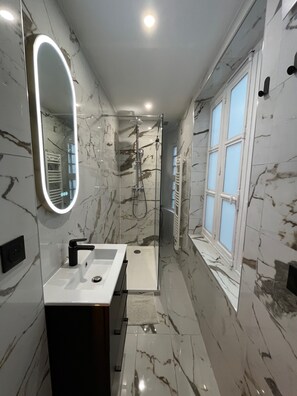 Ein modernes Badezimmer mit Marmorboden, einem großen Spiegel, einer Dusche und einem Fenster.