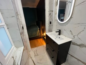 Ein Badezimmer mit weißem Waschbecken, einem schwarzen Schrank und einem Spiegel mit Beleuchtung.