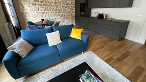 Ein modernes Wohnzimmer mit blauer Couch, Steinwand, Küchenbereich und Esstisch mit Stühlen.