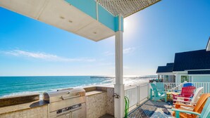 A beachside balcony with a grill, colorful Adirondack chairs, and a view of the ocean and pier. - Big Blue -Mini-Resort, Movie Theater, Pools, Hot Tub, Beach Front, Sleeps 28! (Surf City)