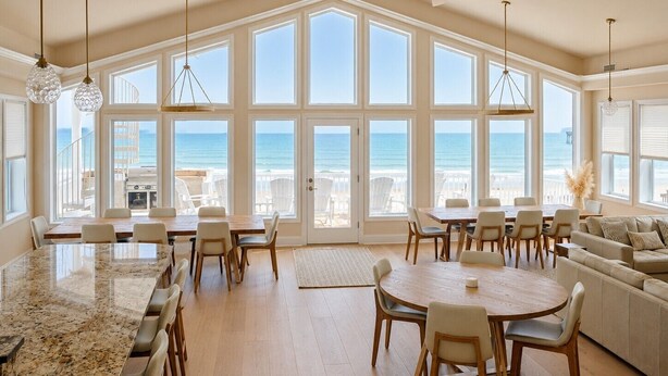 A spacious dining area with large windows, a ceiling fan, and a view of the ocean. - Big Blue -Mini-Resort, Movie Theater, Pools, Hot Tub, Beach Front, Sleeps 28! (Surf City)