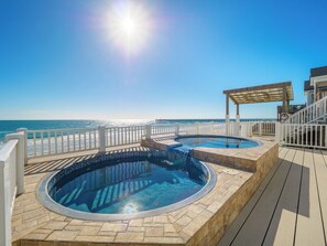 Zona de piscina con dos jacuzzis y una pérgola con vistas a la playa.