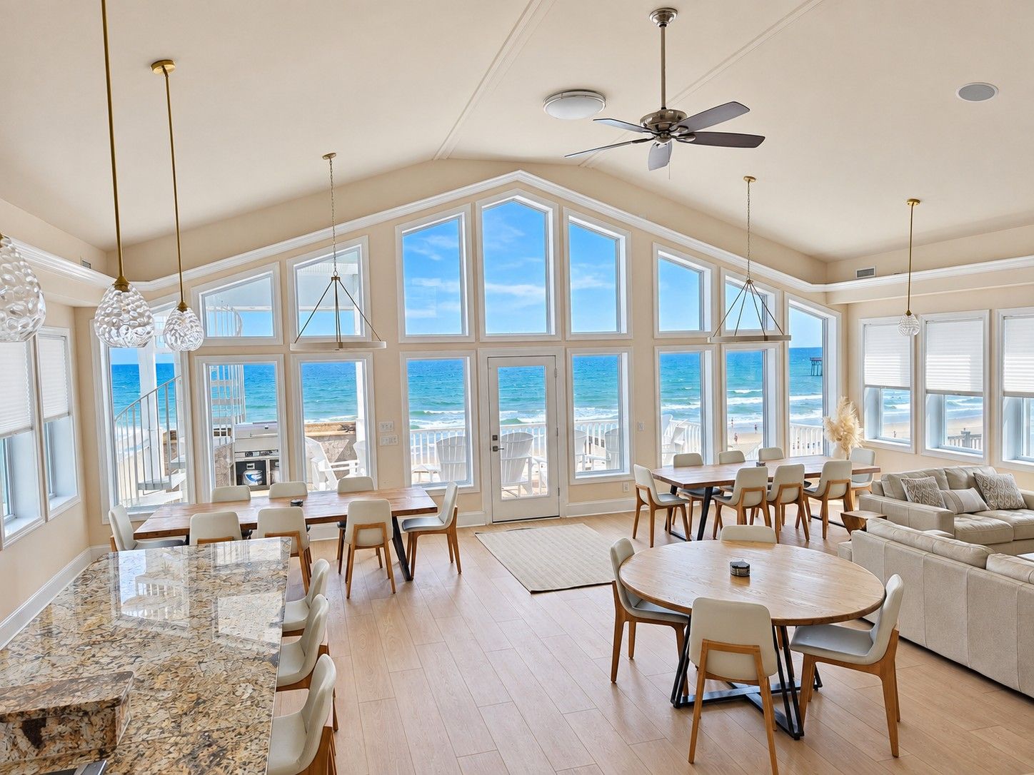 A spacious kitchen with large windows, a ceiling fan, and a variety of seating arrangements.