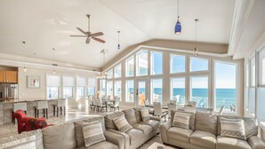 A spacious living area with a large window overlooking the ocean, a ceiling fan, and a dining area with a view. - Big Blue -Mini-Resort, Movie Theater, Pools, Hot Tub, Beach Front, Sleeps 28! (Surf City)