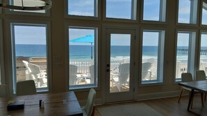 A room with large windows overlooking a beach, white chairs, and a wooden table. - Big Blue -Mini-Resort, Movie Theater, Pools, Hot Tub, Beach Front, Sleeps 28! (Surf City)
