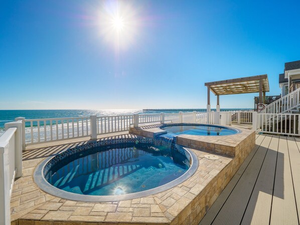 Zona de piscina con dos jacuzzis y una pérgola con vistas a la playa.