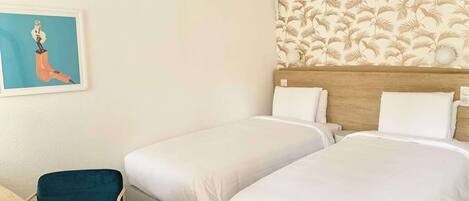 A hotel room with two beds, a wooden headboard, a wall with a palm leaf pattern, and a framed picture on the wall.