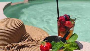 Escena junto a la piscina con un sombrero tejido, un vaso con una bebida y una pajita.