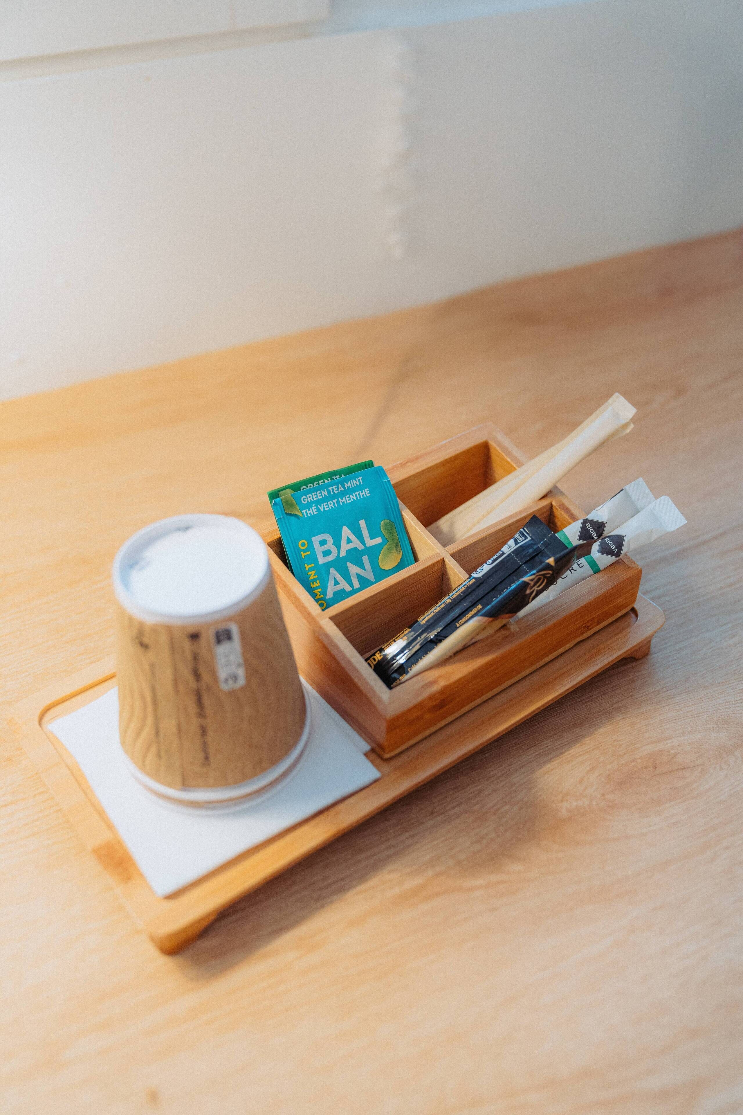Una bandeja de madera con una taza, una caja con la etiqueta "BALAN" y varios objetos sobre una mesa de madera.