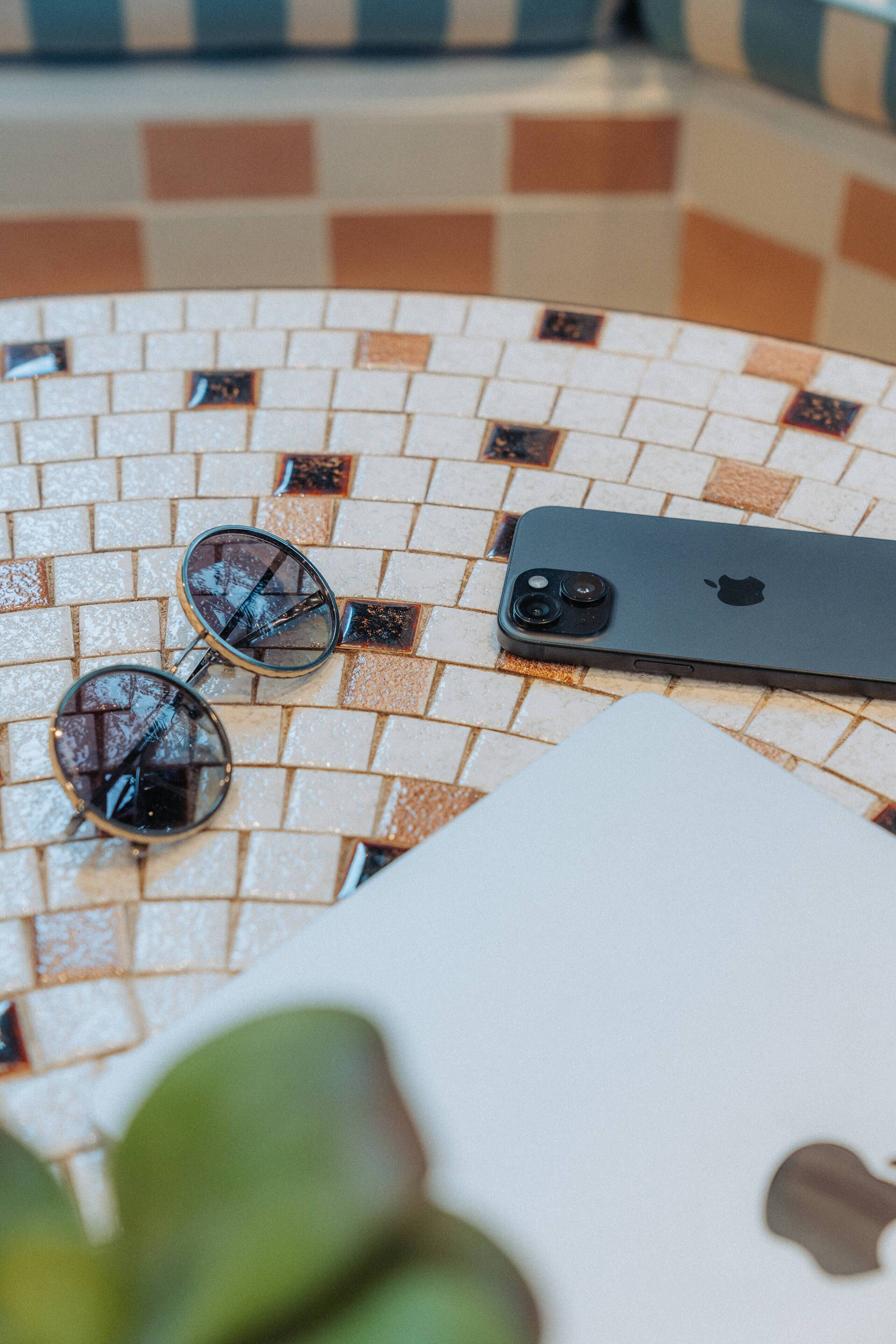 Uno smartphone, un paio di occhiali da sole e un quaderno su un tavolo piastrellato.