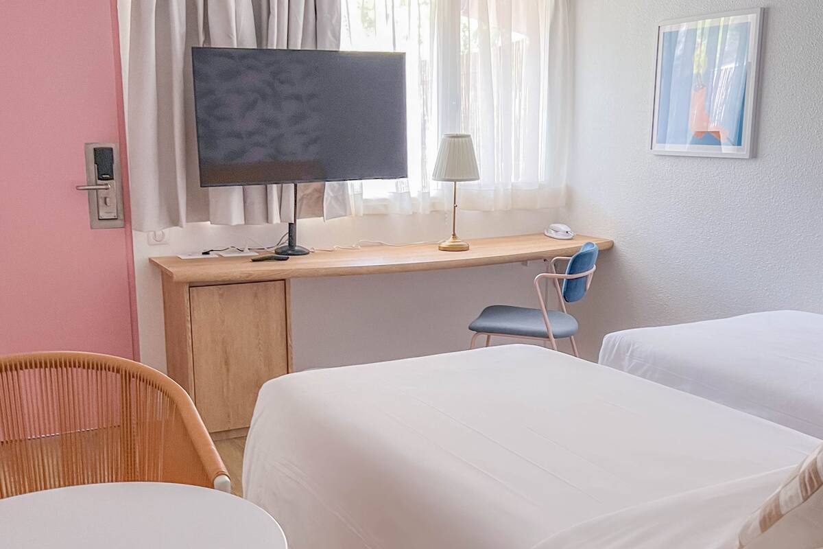 Une chambre d’hôtel avec un bureau en bois, une télévision, une lampe, une chaise et deux lits.