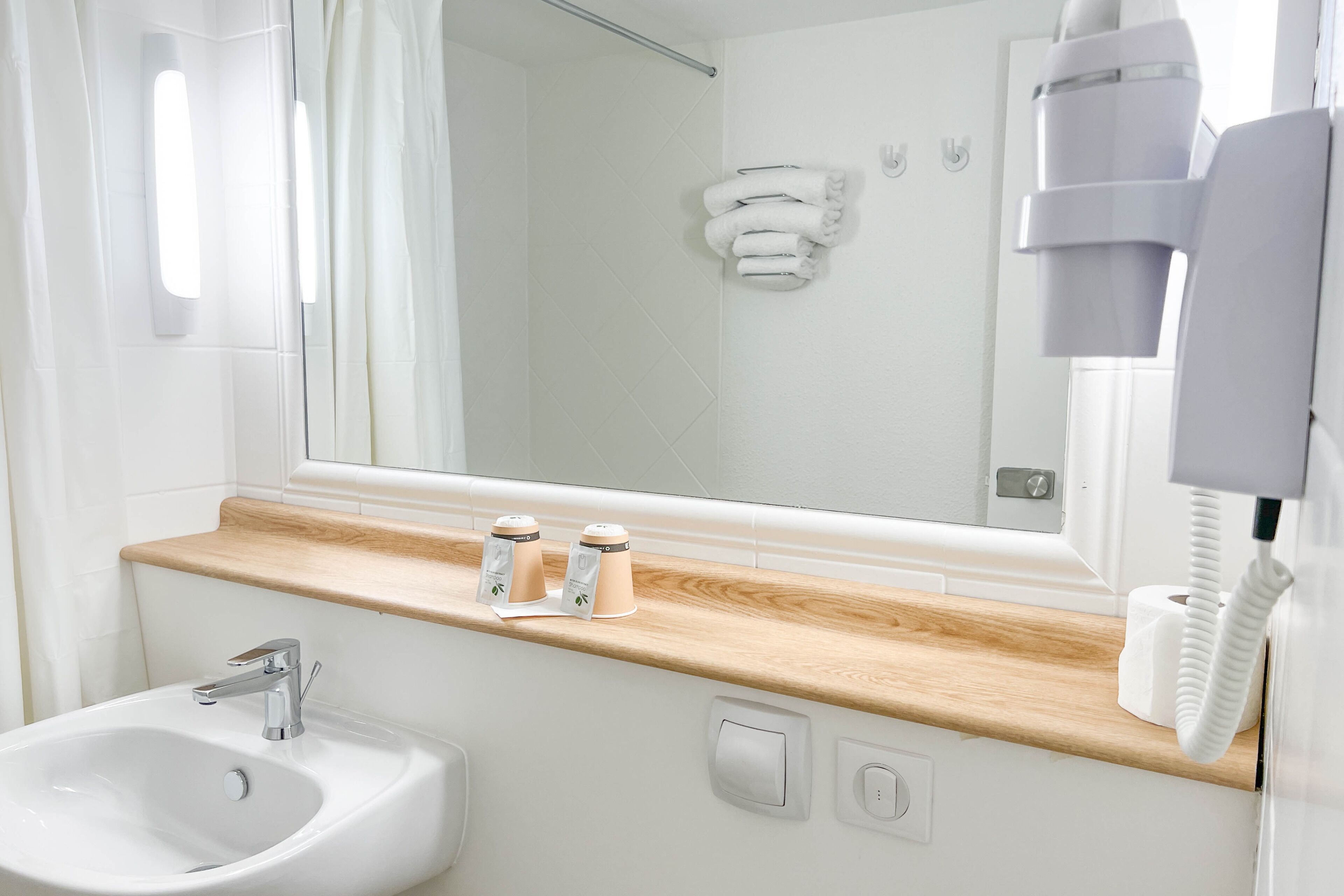 Ein modernes Badezimmer mit einem weißen Waschbecken, einer Holz-Arbeitsfläche und einem großen Spiegel.