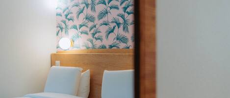 A hotel room with a bed, white bedding, a wooden headboard, and a wall with a tropical leaf pattern.
