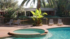 Una piscina con borde de mosaicos, rodeada por una valla y palmeras.