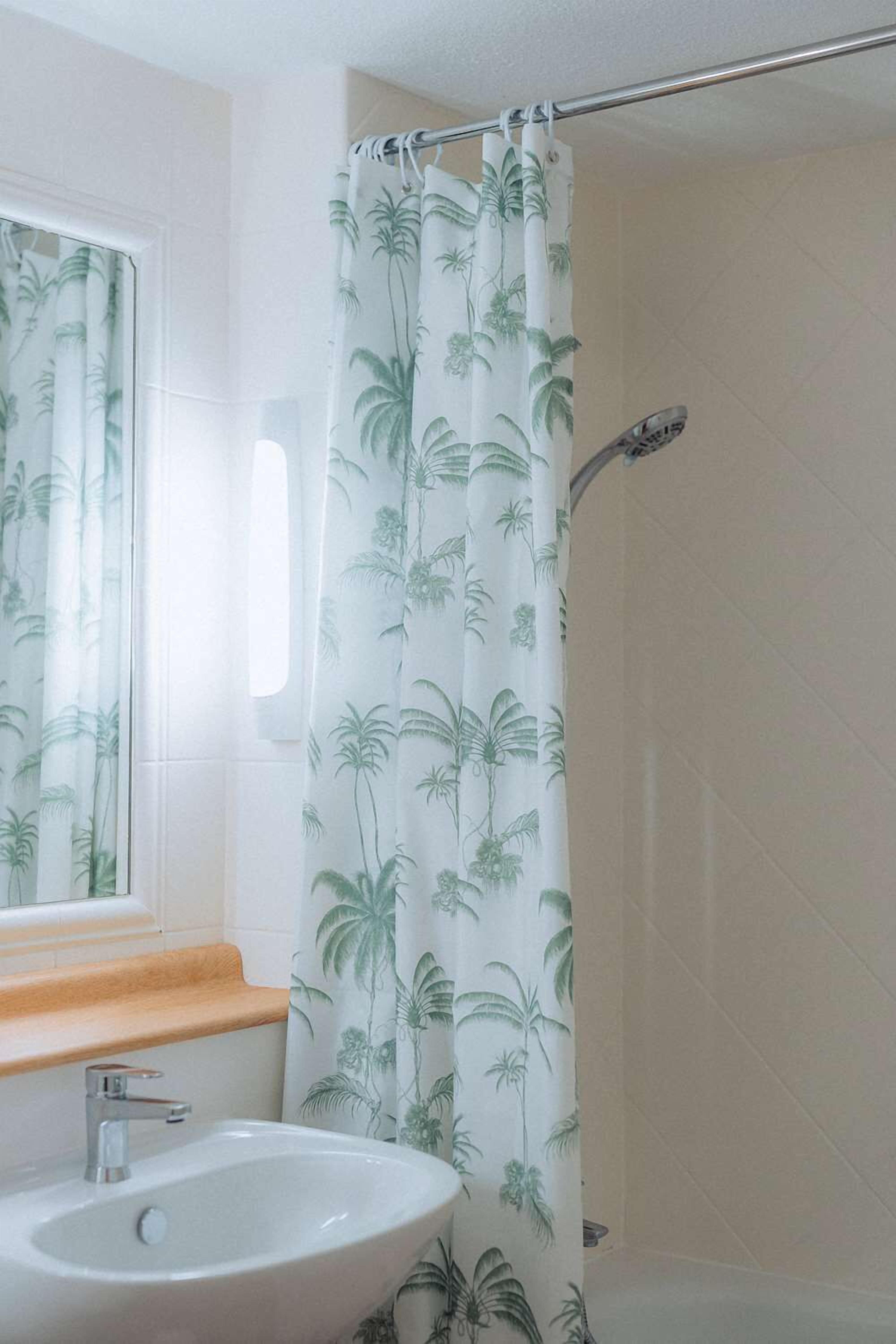 A bathroom with a white sink, a window with a white curtain, and a shower curtain with a palm tree pattern.