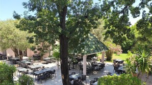 Un área de comedor al aire libre con mesas y sillas, rodeada de árboles y un pabellón cubierto.