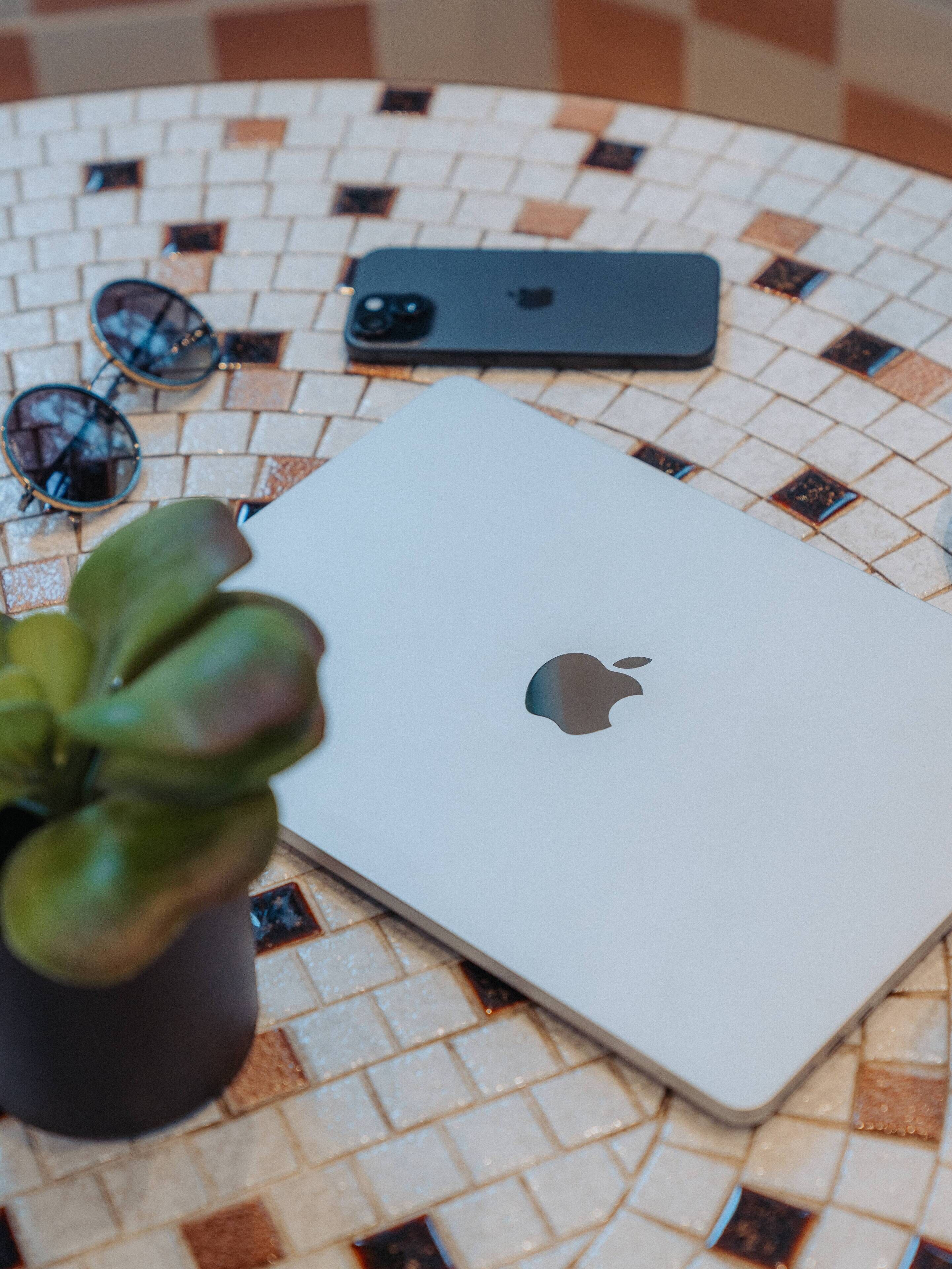 Una computadora portátil, gafas de sol y una planta en maceta sobre una mesa con azulejos.