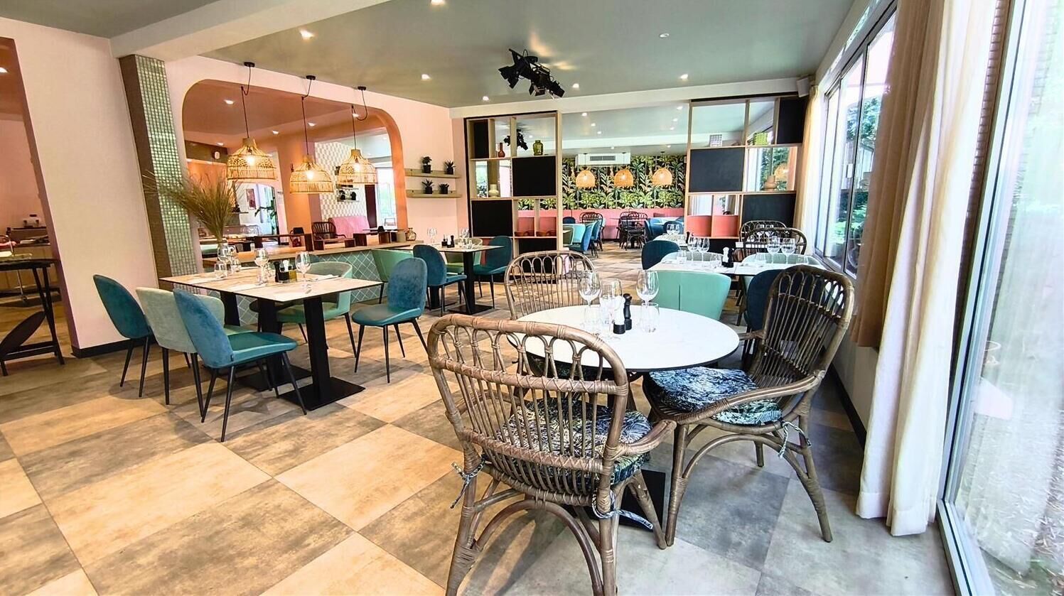 A restaurant with round tables, wicker chairs, and a view of the outdoors.