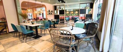 A restaurant with round tables, wicker chairs, and a view of the outdoors.