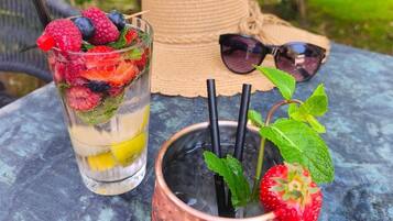 A glass with fruit and a straw, a copper mug with a straw, sunglasses, and a straw hat on a table.