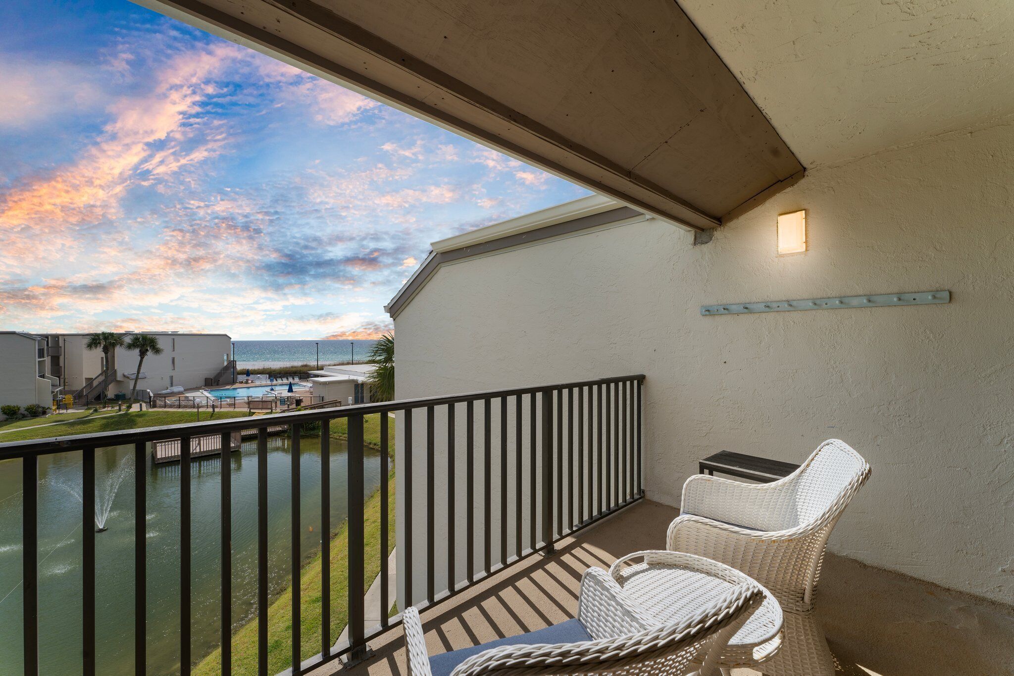 A balcony with wicker furniture, a pool, and a view of the ocean.