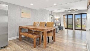 A dining area with a wooden table and chairs, a sofa, and a ceiling fan. - Family-friendly oceanfront escape w/ views steps from private beach (Panama City Beach)