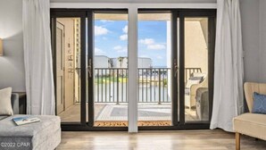 A room with a sliding glass door leading to a balcony with a view of a building and a garden. - Family-friendly oceanfront escape w/ views steps from private beach (Panama City Beach)