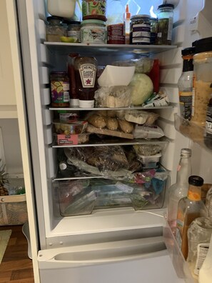 A refrigerator stocked with various food items including jars of condiments, packaged meats, and a bottle of beer.