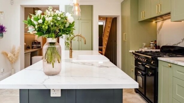 Una cocina moderna con una isla central, gabinetes verdes y un tragaluz.
