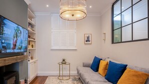 Una sala de estar con un sofá gris, televisor, chimenea y un ventanal con persianas.