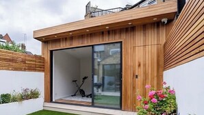 A modern house with a wooden exterior, a glass door leading to a garage, and a well-maintained lawn. - 3 bedroom 3 story House & Garden 
AIR CONDITIONING (London)
