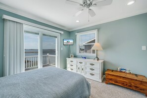 A bedroom with a bed, a dresser, a wooden bench, a ceiling fan, and a TV on the wall.