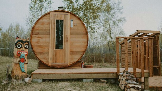 Una baita in legno con un'ampia porta centrale, un piccolo portico e una scultura totemica.