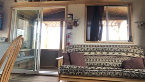 Un accogliente soggiorno con un divano, una sedia di legno, una porta vetrata che dà sull'esterno e una finestra con tende.